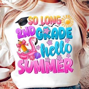 Op de afbeelding: Witte trui met de tekst "So Long 2nd Grade Hello Summer" in kleurrijke letters. Het ontwerp bevat een afstudeerpet, een flamingo op een zwemband, een potlood en een zon.