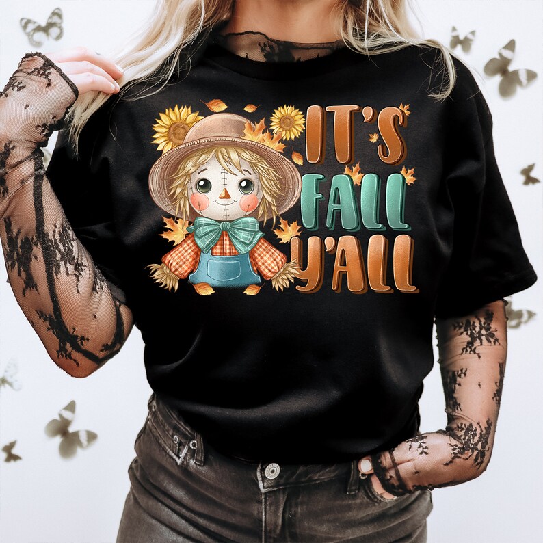 Op de afbeelding: Zwart T-shirt met een cartoon-vogelverschrikker die een bruine hoed en een geruit overhemd draagt. De tekst "It's Fall Y'all" staat op het shirt gedrukt.
