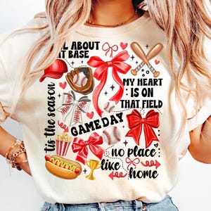 以下が含まれることがあります： 野球をテーマにした白いTシャツ。Tシャツには、赤いリボン、野球のバット、野球グローブ、野球ボール、ポップコーン、ホットドッグ、トロフィー、そして「All about it base」、「Tis the season」、「My heart is on that field」、「Game day」、「No place like home」の文字が書かれています。