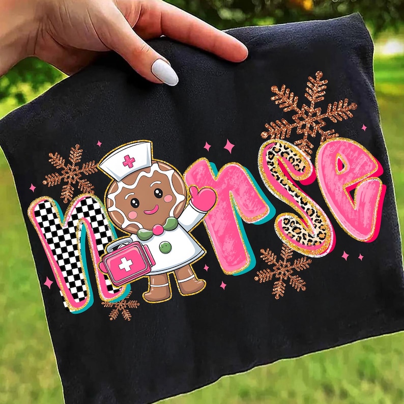 May include: Black fabric with the word "NURSE" in pink, gold, and checkered letters, featuring a gingerbread nurse with a pink medical bag and snowflakes. The design is held by a hand.