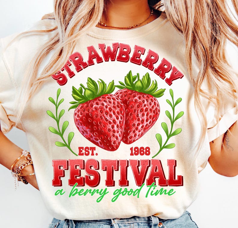 May include: A white t-shirt with a red graphic that says "Strawberry Festival Est. 1968 a berry good time". The graphic also features two red strawberries with green leaves.