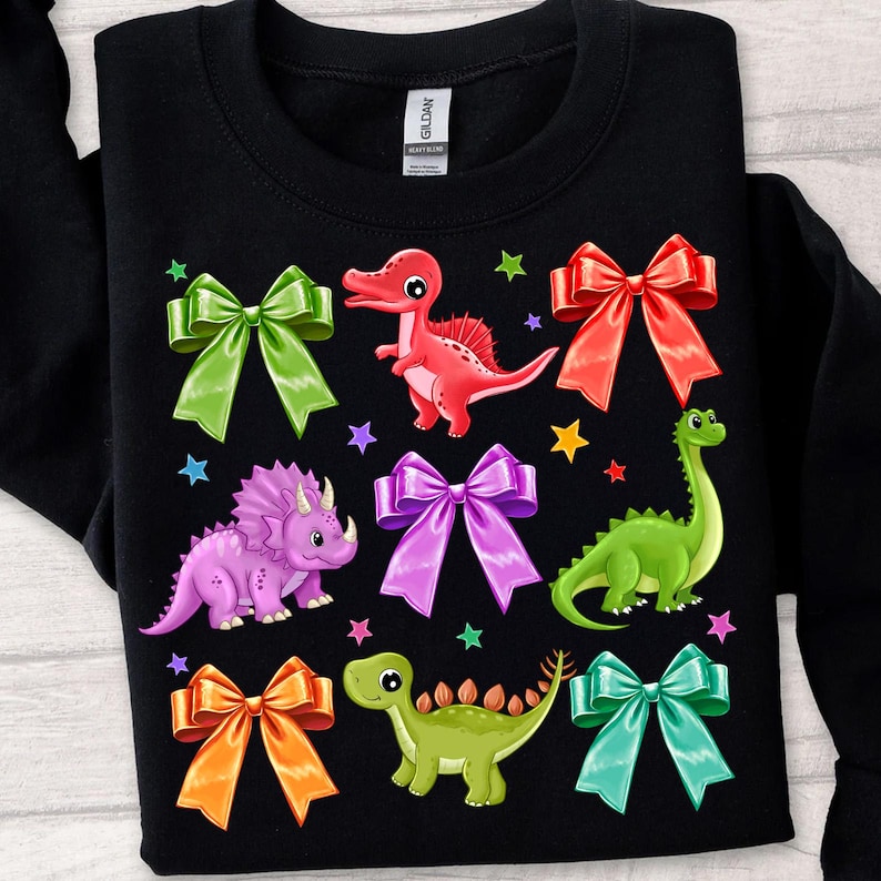 May include: Black sweatshirt with a colorful dinosaur and bow design. The dinosaurs are green, purple, red, and green. The bows are red, green, purple, orange, and teal.