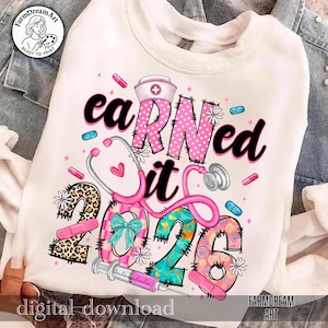 May include: White sweatshirt with the text "earned it 2026". The design includes a nurse's hat, stethoscope, pills, and a syringe. The numbers 2026 are decorated with patterns and a bow.