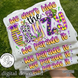 May include: White t-shirts stacked, featuring the text "We don't hide the crazy, we parade it" in yellow, purple, and green. The design includes a crown, masks, and fleur-de-lis, perfect for Mardi Gras celebrations.