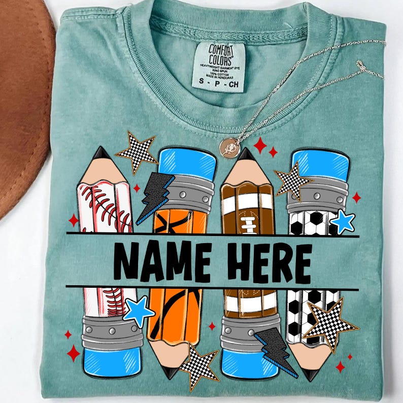 Pode incluir: Uma camiseta Comfort Colors verde-azulado com um design de l&aacute;pis com bolas esportivas e um raio. O texto "NAME HERE" &eacute; impresso em negrito preto. Um colar de prata com um pingente tamb&eacute;m &eacute; vis&iacute;vel.