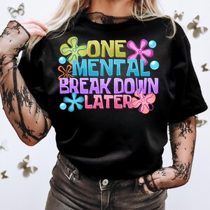 May include: Black t-shirt with a colorful graphic that says "One Mental Break Down Later" with flower-like designs.