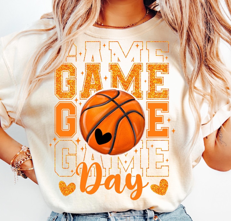 Peut inclure: T-shirt blanc avec un motif de ballon de basket orange et noir et le texte "Game Day" en lettres orange paillet&eacute;es.