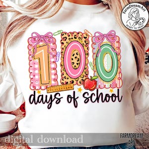 May include: White sweatshirt with a colourful graphic celebrating 100 days of school. The design features the numbers "100" in pink, green, and leopard print, with bows, paperclips, and an apple. The words "days of school" are written in black script.