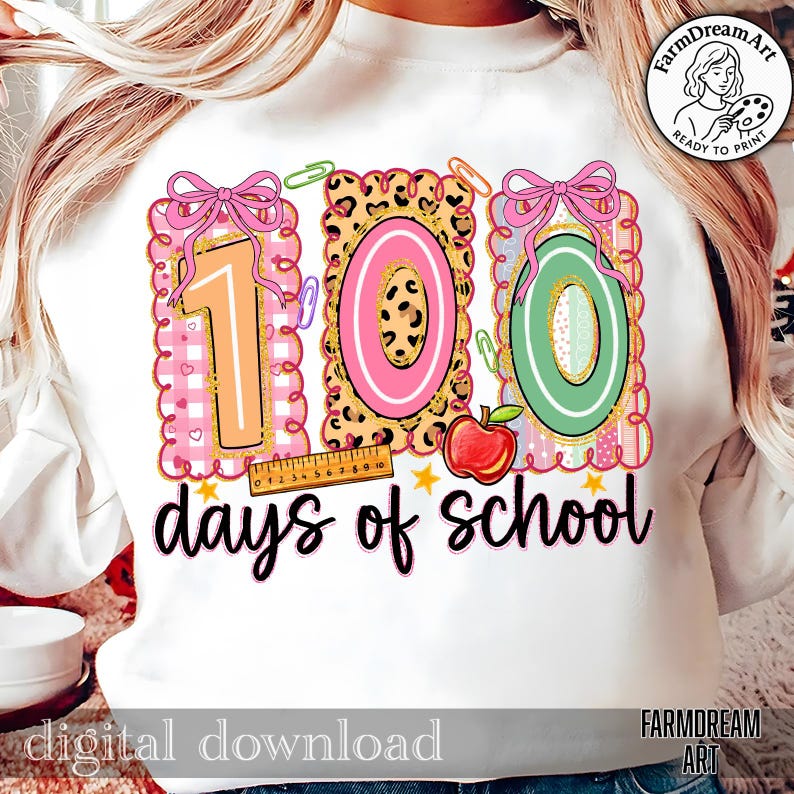 May include: White sweatshirt with a colourful graphic celebrating 100 days of school. The design features the numbers "100" in pink, green, and leopard print, with bows, paperclips, and an apple. The words "days of school" are written in black script.
