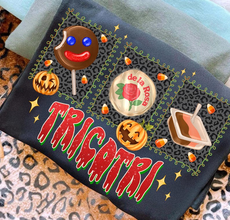 K&ouml;nnte beinhalten: Dunkelblaues T-Shirt mit einem Halloween-Motiv. Das Shirt zeigt einen Lebkuchenmann-Lutscher, K&uuml;rbisse, Zuckermais und das Wort "TRICKORTREAT" in roter und gr&uuml;ner Schrift. Das Design ist von einem Leopardenmuster umgeben.