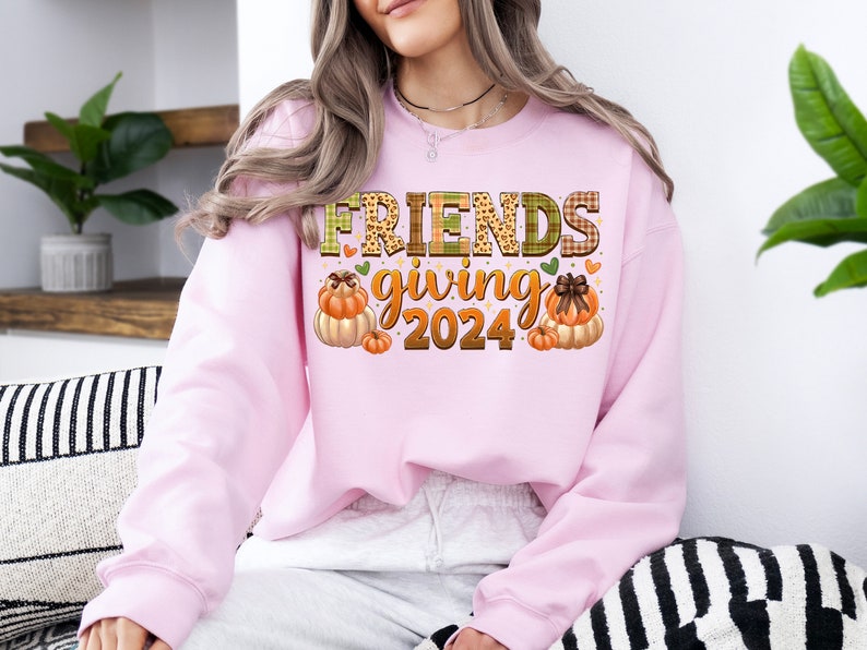 May include: Pink sweatshirt with the text "Friendsgiving 2024" in a plaid and leopard print font. The text is surrounded by small hearts and two illustrations of pumpkins.