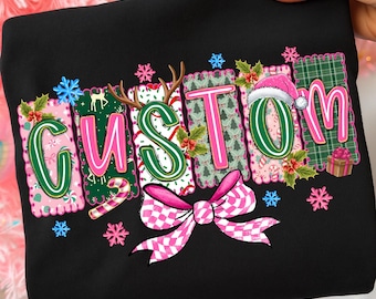 May include: Black sweatshirt with the word "CUSTOM" in a festive, colorful design. The letters are decorated with Christmas elements like snowflakes, antlers, a Santa hat, and a pink bow. The design is set against a backdrop of pink and green patterns.