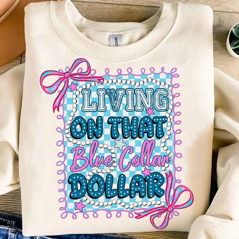 Pu&ograve; includere: Felpa color crema con la scritta "LIVING ON THAT Blue Collar DOLLAR" in blu e rosa. Il testo &egrave; incorniciato da un motivo a scacchi blu e bianco, fiocchi rosa e stelle.
