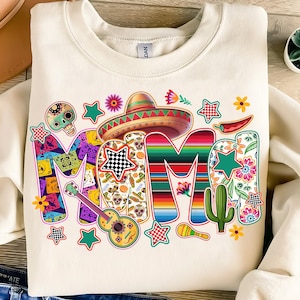 Op de afbeelding: Een wit sweatshirt met een kleurrijk ontwerp dat "Mama" zegt in een feestelijk lettertype. Het ontwerp bevat een sombrero, bloemen, sterren en een cactus.