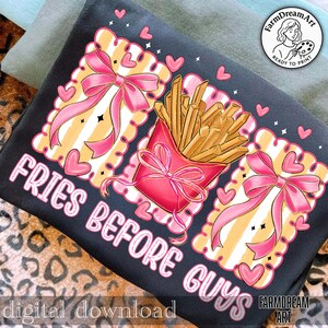 Op de afbeelding: Zwart t-shirt met een grafisch ontwerp. Het heeft een rode bak friet, roze strikken en de tekst "FRIES BEFORE GUYS". Het ontwerp bevat roze harten en een decoratieve rand met een gestreepte achtergrond.