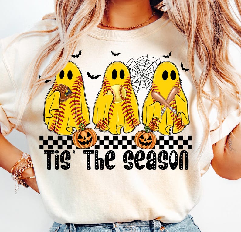 Puede incluir: Sudadera color crema con tres figuras de fantasmas amarillos con costuras de b&eacute;isbol, sosteniendo una pelota, un bate y un guante. Murci&eacute;lagos negros y una telara&ntilde;a est&aacute;n encima de los fantasmas. El texto "Tis' The Season" est&aacute; debajo, con calabazas.