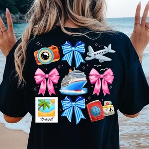 Puede incluir: Camiseta negra con un dise&ntilde;o colorido de tem&aacute;tica de viaje. El dise&ntilde;o incluye una c&aacute;mara, un crucero, un avi&oacute;n, un pasaporte, una palmera y lazos en azul, rosa y blanco.