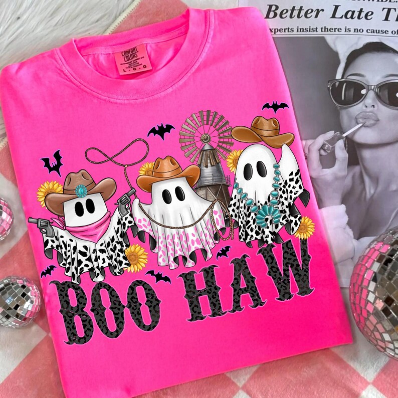 May include: A hot pink Comfort Colors t-shirt featuring a graphic of three ghost characters dressed as cowboys, with cowboy hats, bandanas, and cow-print accents. The text "BOO HAW" is printed in a black, leopard-print font. Bats and sunflowers are also included in the design.