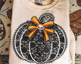 Może przedstawiać: Beżowa bluza z motywem dyni na Halloween. Dynia wykonana jest z czarnej koronki z białymi konturami i czarną koronkową obwódką. Pomarańczowa i czarna kokarda z czaszką dopełnia design, idealny na Halloween.