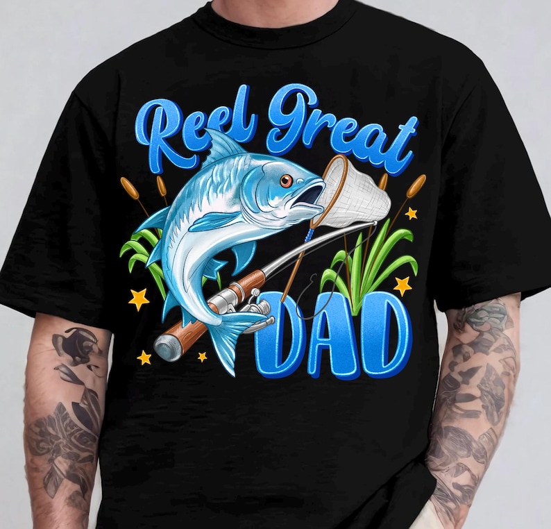 May include: Black t-shirt with a blue graphic of a fish, fishing rod, and the words "Reel Great Dad." The fish is light blue with orange accents. The text is in a stylized font with a blue gradient.