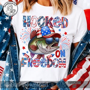 May include: White t-shirt with a graphic of a fish wearing sunglasses and a patriotic hat. The text "HOOKED ON FREEDOM" is displayed in red, white, and blue. Fireworks and stars complete the design.