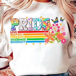 Könnte beinhalten: Weißes Sweatshirt mit dem Wort "PRIDE" in bunten, gemusterten Buchstaben. Darunter stehen die Worte "LOVE, RESPECT, FREEDOM, TOLERANCE, DIVERSITY" auf einem Regenbogenstreifen. Das Design umfasst Blumen, Schmetterlinge und Sterne.