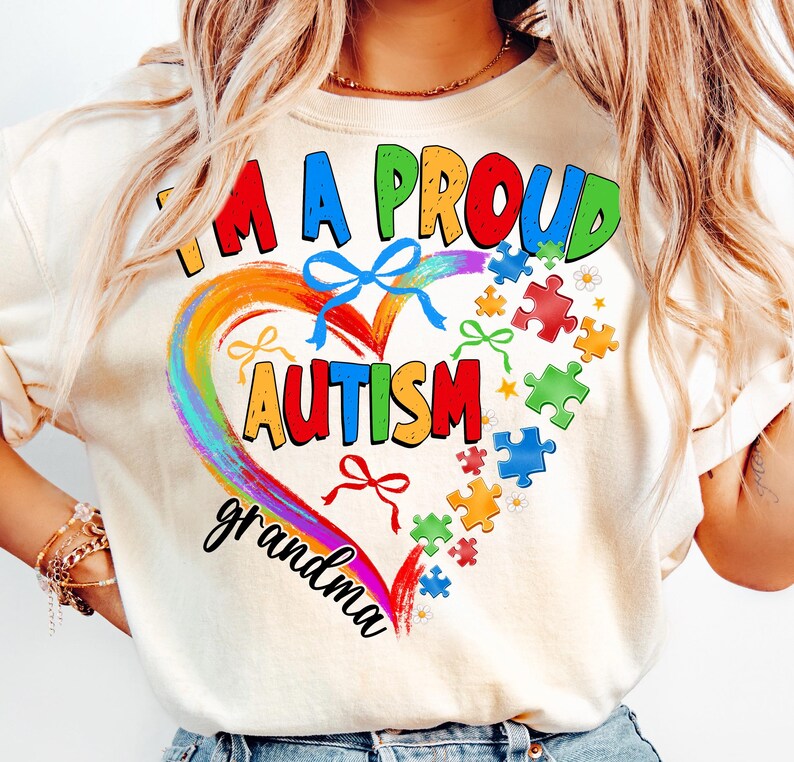 May include: A white t-shirt with a rainbow heart design and the text "I'm a proud autism grandma". The heart is surrounded by puzzle pieces and bows.