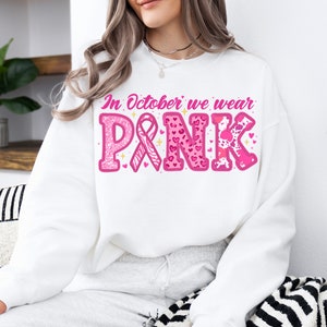 May include: White sweatshirt with the text "In October we wear PINK" in pink letters with pink ribbon, hearts, and animal print designs.