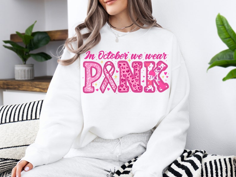 May include: White sweatshirt with the text "In October we wear PINK" in pink letters with pink ribbon, hearts, and animal print designs.