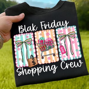 May include: Black t-shirt with the words "Blak Friday Shopping Crew" in white script. The shirt features three colorful rectangular designs with bows, stripes, and shopping-themed graphics, including a shopping cart and gift boxes.