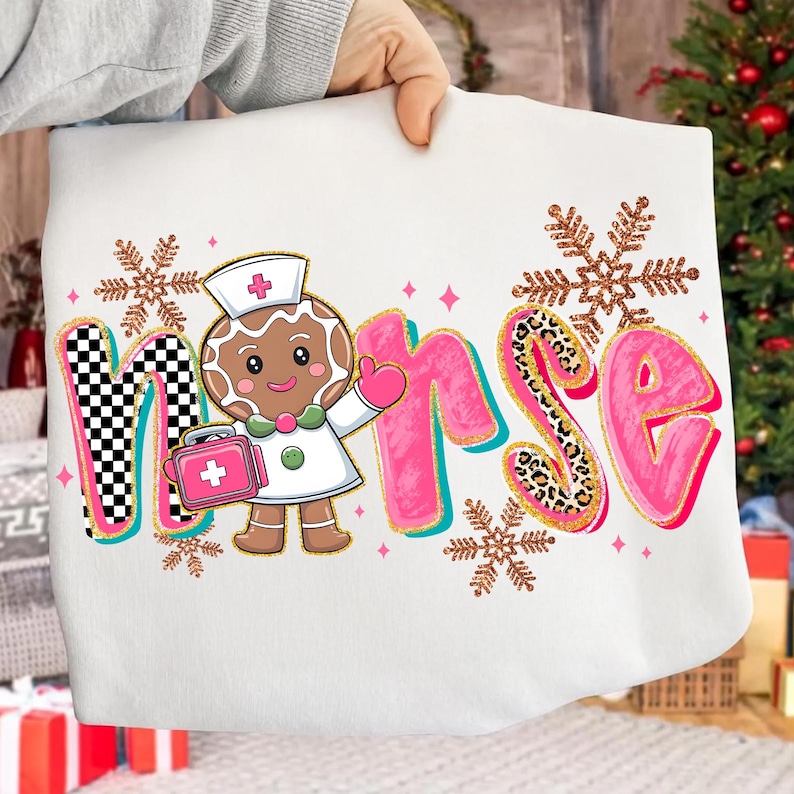 May include: White sweatshirt featuring the word "Nurse" in pink, teal, and leopard print, with a gingerbread nurse graphic. The design includes snowflakes and a checkered pattern, creating a festive, holiday-themed look.