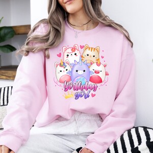 Puede incluir: Sudadera rosa con un gr&aacute;fico de adorables animales de dibujos animados, incluyendo un unicornio, un gato y un conejito. El texto "birthday girl" est&aacute; impreso en la sudadera.