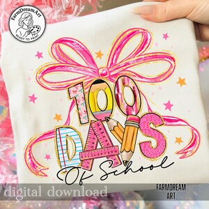 May include: A cream-colored t-shirt with a colorful graphic design celebrating 100 days of school. The design includes a pink bow, stars, and the text "100 Days Of School". The words "digital download" and "FarmDreamArt" are also visible.