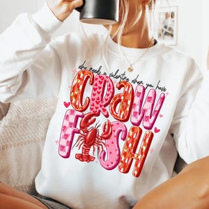 May include: White sweatshirt with a red and pink graphic that says "Who needs a valentine when you have crawfish" with a red crawfish illustration.