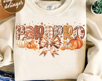 May include: A beige sweatshirt with a design of the word "papparo" in brown, orange, and white patterned letters with a brown and gold bow and pumpkins.