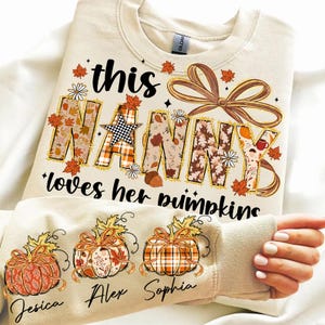 May include: Cream-colored sweatshirt with the text "this Nanny loves her pumpkins." The word "Nanny" is decorated with fall-themed patterns. The sleeves feature pumpkin graphics with names below them.