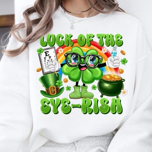 May include: White sweatshirt with a green shamrock cartoon character wearing glasses and holding a pot of gold. The text "Luck of the Eye-rish" is printed on the shirt.