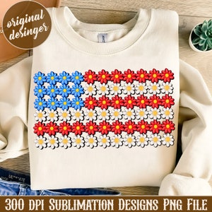 May include: A white sweatshirt with a design of an American flag made of red, white, and blue daisies. The design is centered on the sweatshirt.