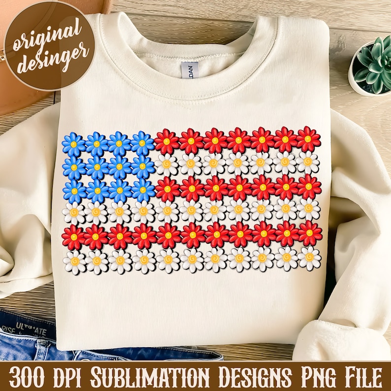 May include: A white sweatshirt with a design of an American flag made of red, white, and blue daisies. The design is centered on the sweatshirt.