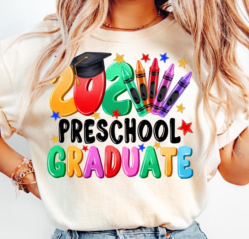 May include: A white t-shirt with a colorful graphic design that says "2023 Preschool Graduate". The design features a graduation cap, crayons, and stars.
