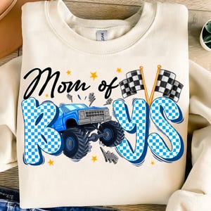 May include: A white sweatshirt with a blue and white checkered graphic that says "Mom of Boys". The graphic also includes a blue monster truck with checkered flags.