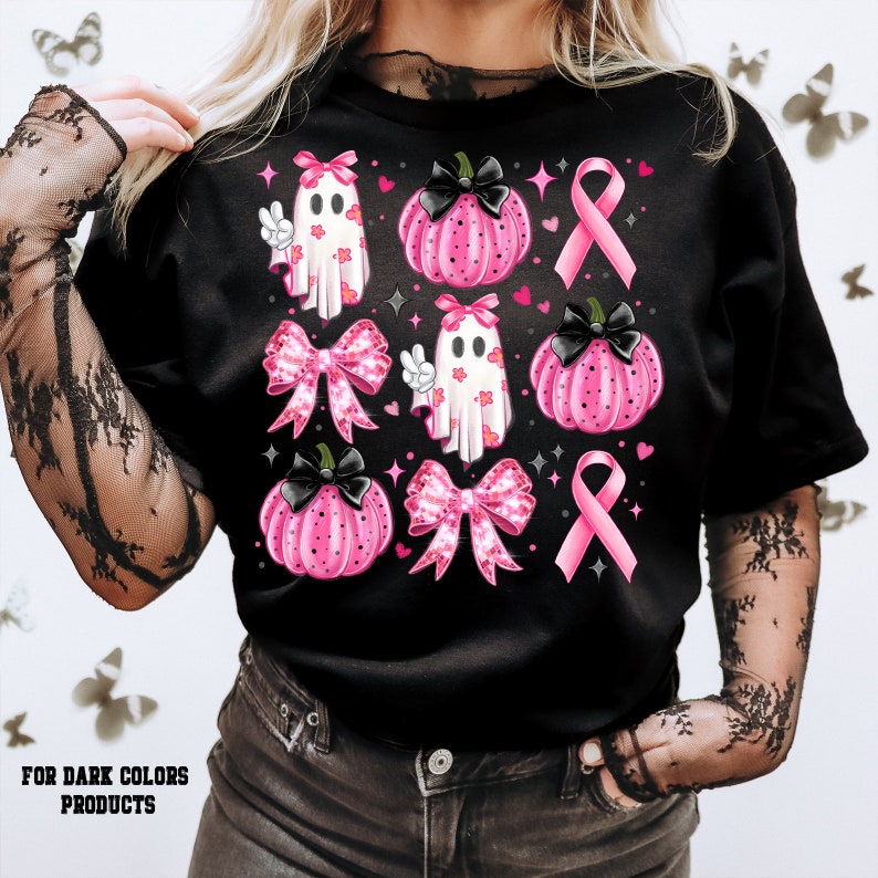 以下が含まれることがあります： ピンクのリボン、ゴースト、カボチャが描かれた黒いTシャツ。デザインには、ピンクのリボン、ピースサインをしたゴーストが2体、黒い茎とピンクのドット模様のカボチャが3つ描かれています。デザインはピンクのリボンとハートで囲まれています。
