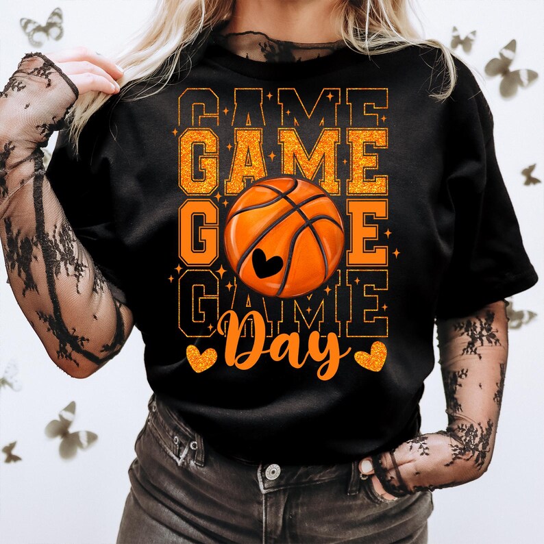 Peut inclure: T-shirt noir avec un texte en paillettes orange qui dit "Game Game Go Game Day" avec un graphique de ballon de basket orange au centre.