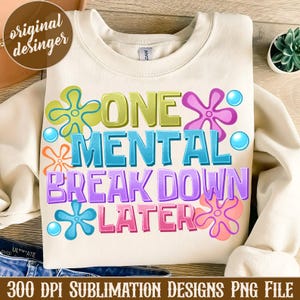 May include: A white sweatshirt with a colorful graphic design that says "One Mental Break Down Later". The graphic features a cartoon-style design with colorful flowers and bubbles.