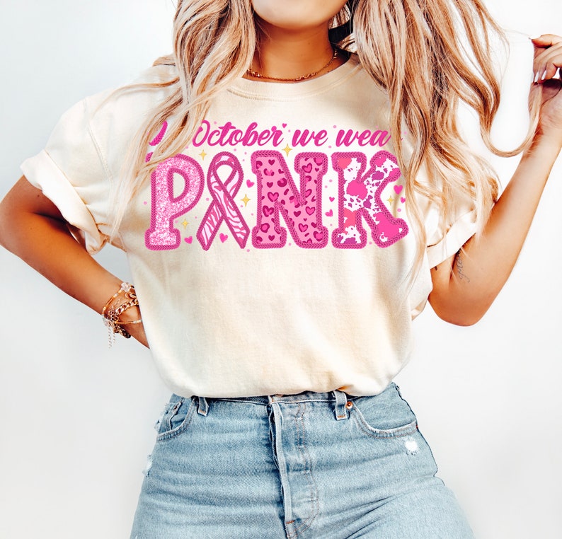 May include: A white t-shirt with the text "In October we wear PINK" in pink letters with glitter and pink ribbon, hearts, and animal print designs.
