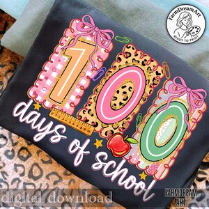 May include: A dark grey t-shirt with a vibrant graphic celebrating "100 days of school." The design incorporates the numbers "100" in diverse patterns, a ruler, an apple, and the words "days of school" in a script font. The words "digital download" are also present.
