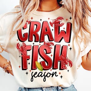 May include: A white t-shirt with red text that says "Crawfish season" with illustrations of crawfish and corn.