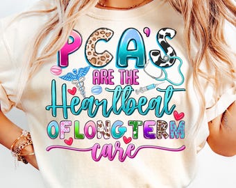May include: Cream-colored t-shirt with the text "PCA's are the Heartbeat of Long Term Care." The text features various colors and patterns, including leopard print and a stethoscope graphic. The shirt also has medical-themed graphics.