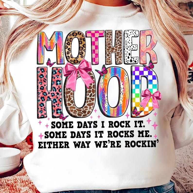 May include: White sweatshirt with a colorful graphic that says "MOTHERHOOD" with a pink bow and butterflies. The text below the graphic says "SOME DAYS I ROCK IT. SOME DAYS IT ROCKS ME. EITHER WAY WE'RE ROCKIN'."