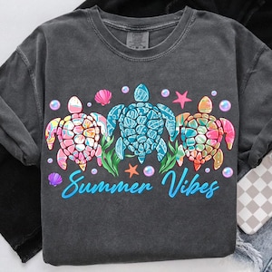 May include: A dark gray t-shirt with a design of three colorful sea turtles with the text "Summer Vibes" in blue.